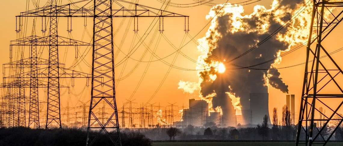 Strommasten und Stromleitungen vor einem Kohlekraftwerk bei Sonnenaufgang: Durch das sogenannte Freileitungsmonitoring soll die Strom-Kapazität der Leitungen verbessert werden.