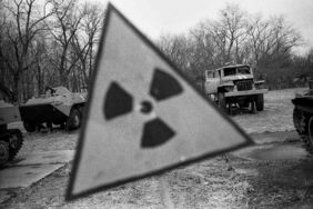 Tschernobyl-Sperrzone: Ein Schild warnt vor Radioaktivität. Im Hintergrund stehen zurückgelassene Militärfahrzeuge. Foto: Arthur Bondar.