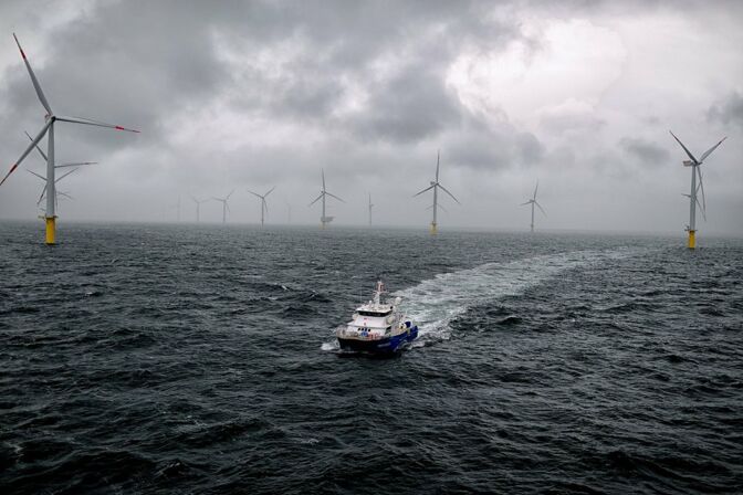 Offshore Windpark Riffgat: Ein Katamaran mit Technikern fährt unter dramatischem Himmel durch die Windräder.