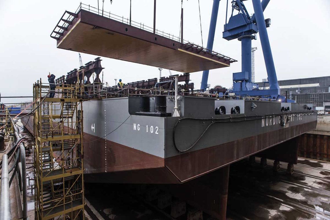 Bau der Konverterstation Dolwin gamma bei Nordic Yards in Warnemünde: Ein Kran hebt eine fast 200 Tonnen schwere Rumpfsektion auf eine Barge.