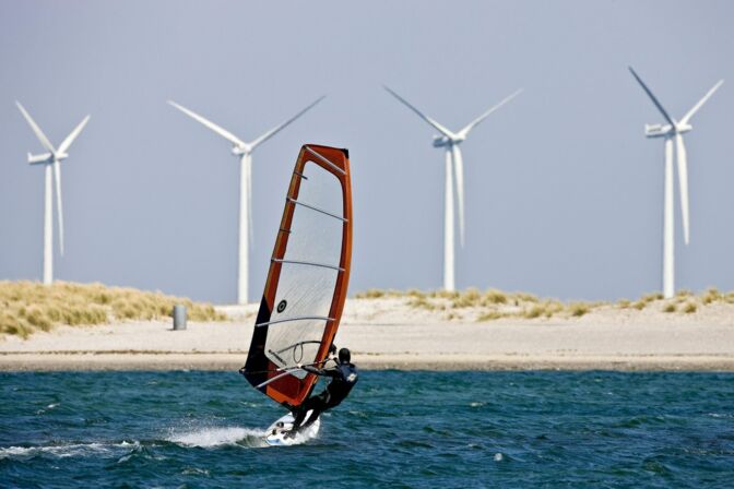 Ein Windsurfer hält auf den Strand von Hvide Sande zu. Im Hintergrund erheben sich Windräder.