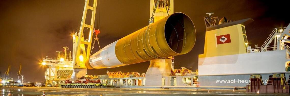 Verladung des Fundaments (Monopile) eines Offshore-Windrads auf ein Schwerlastschiff.