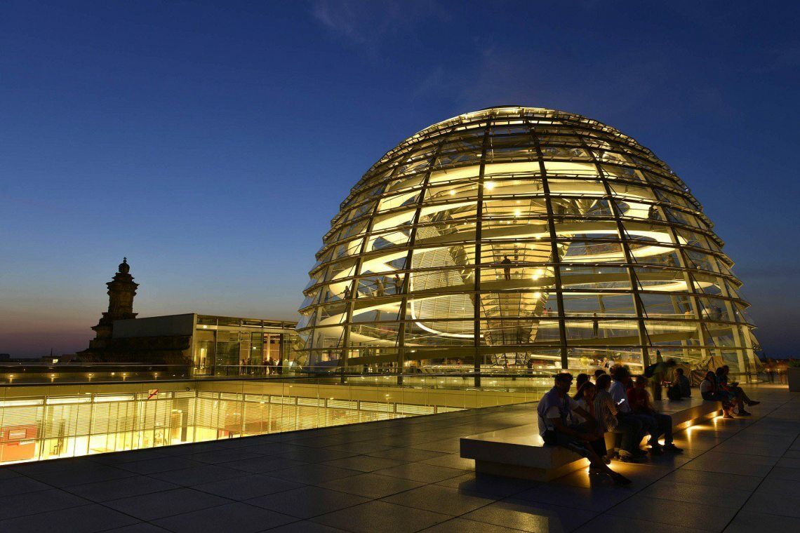 Dach des Reichstags bei Nacht: Besucher sitzen vor der erleuchteten Glaskuppel.