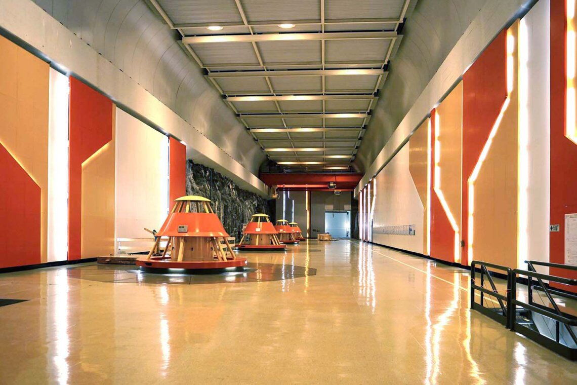 Tief im Inneren des Bergs liegt die gewaltige Kammer des Kraftwerks Kvilldal, 100 Meter lang, 20 Meter hoch. Die zylindrischen Aufbauten gehören zu den Turbinen. Gemeinsam mit den orange verkleideten Wänden und den gezackten Lichtröhren verleihen sie dem