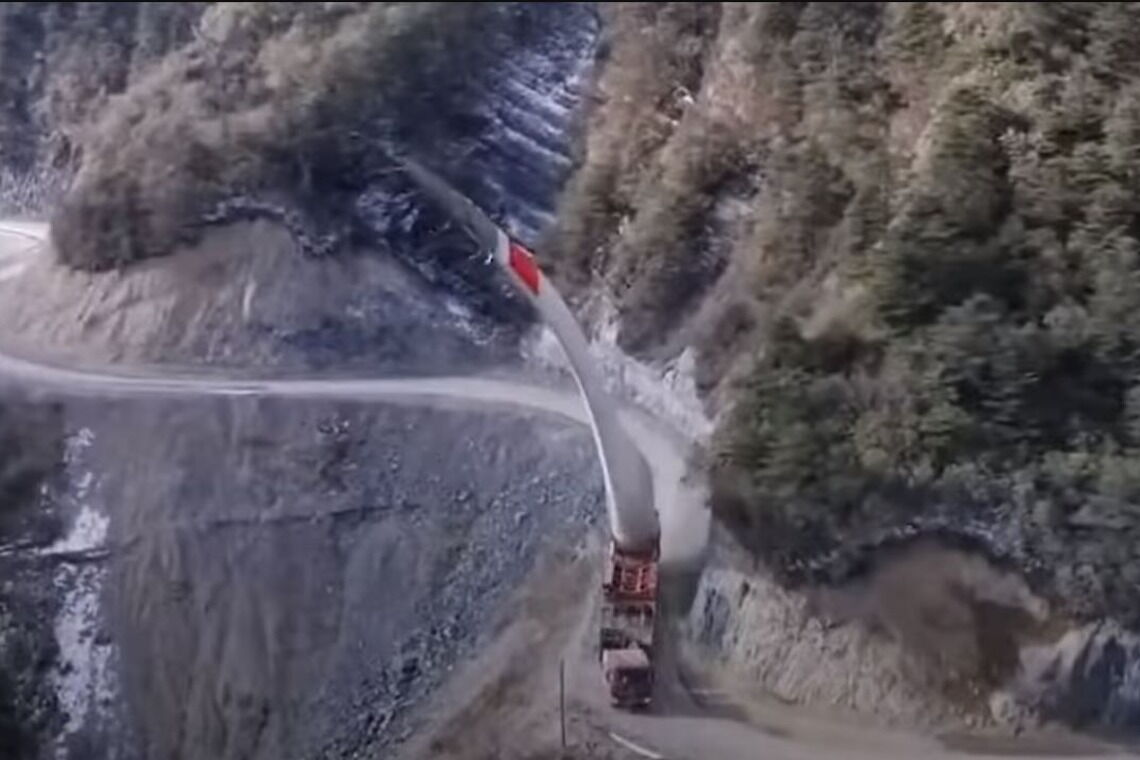 Ein Windrad-Flügel wird an einer Steilwand in China entlang zur Baustelle transportiert. Das Rotorblatt ragt dabei teils weit über den Hang hinaus.