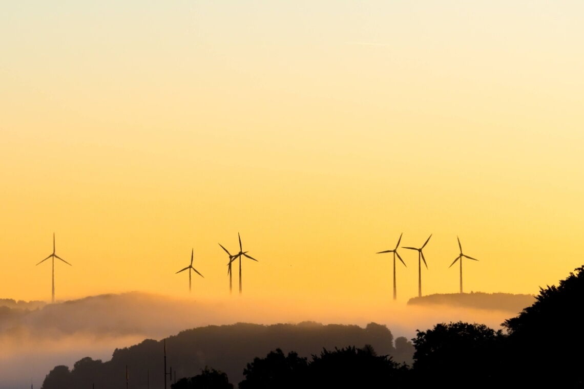Romantische Kulisse: Windräder bei Sonnenaufgang auf nebelverhangenen Hügeln.