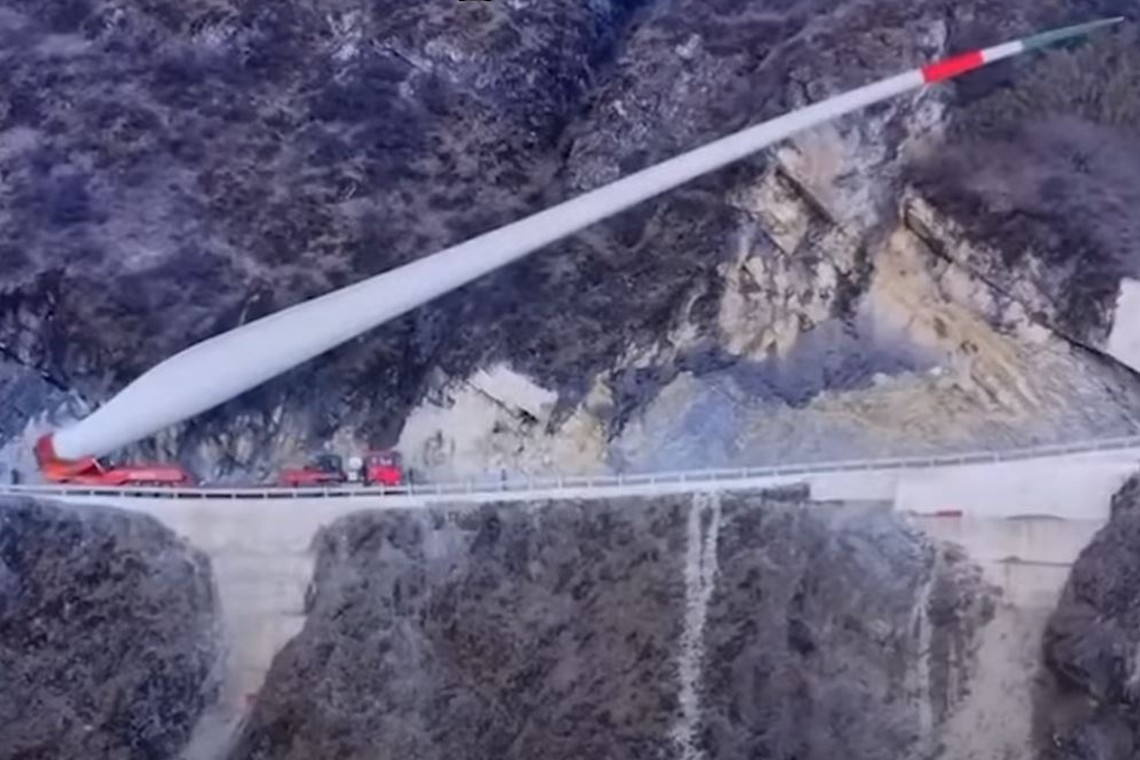 Ein Windrad-Flügel wird an einer Steilwand in China entlang zur Baustelle transportiert. Das Rotorblatt ragt dabei teils weit über den Hang hinaus.